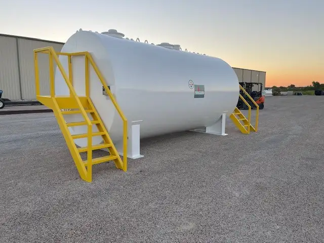 White above ground fuel storage tank with yellow steel access stairs and platforms on both ends, photographed at dusk