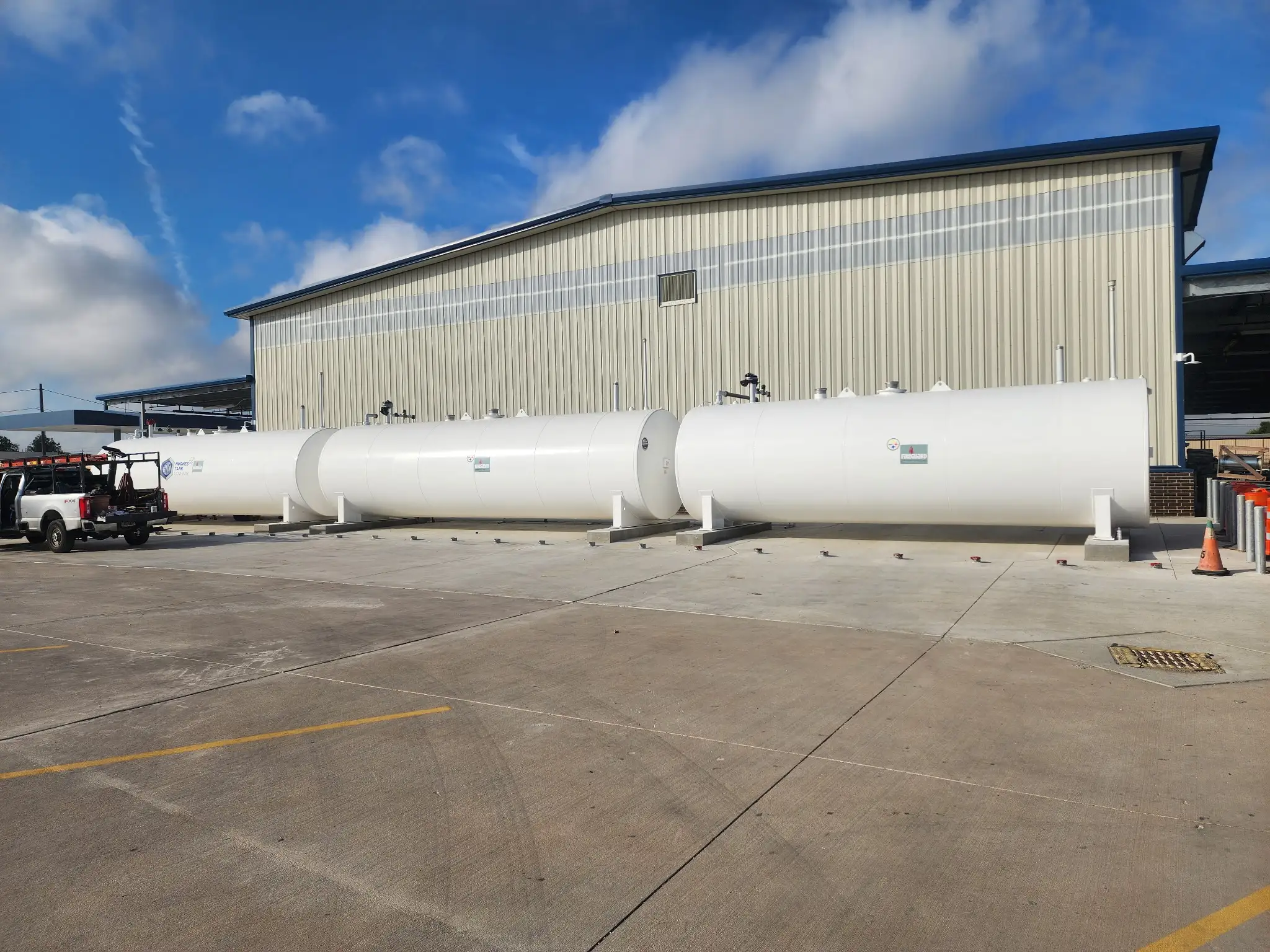 A row of white above ground fuel storage tanks installed on a new concrete pad beside a school district maintenance building