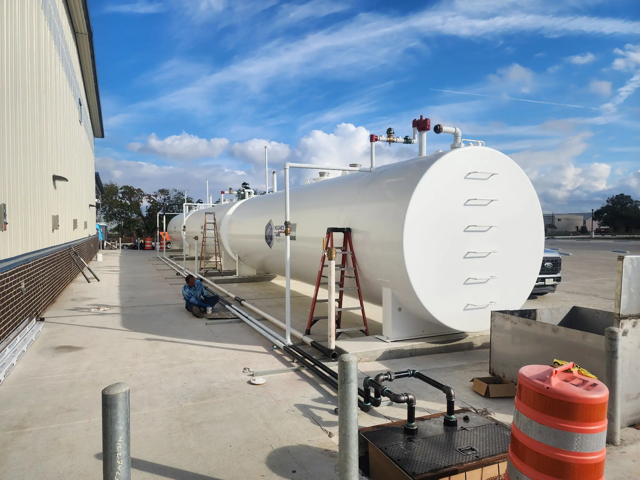 Close view of the installed tank line showing painted access ladders and product piping laid along the pad