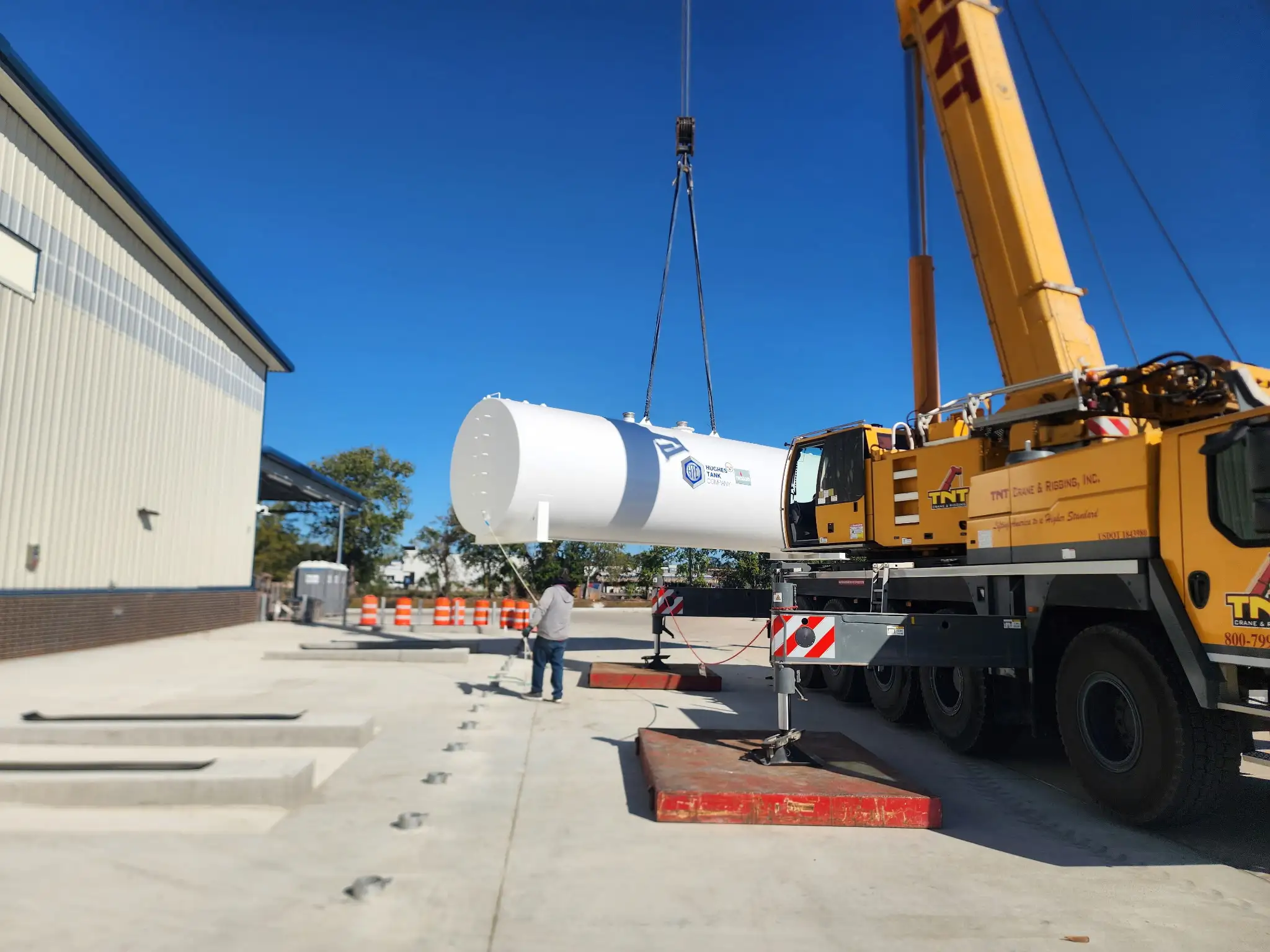 A crane lifts a new above ground storage tank into place beside the building during installation